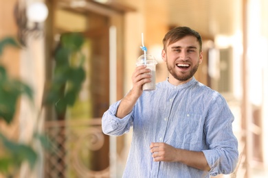 Young man with cup of delicious milk shake outdoors