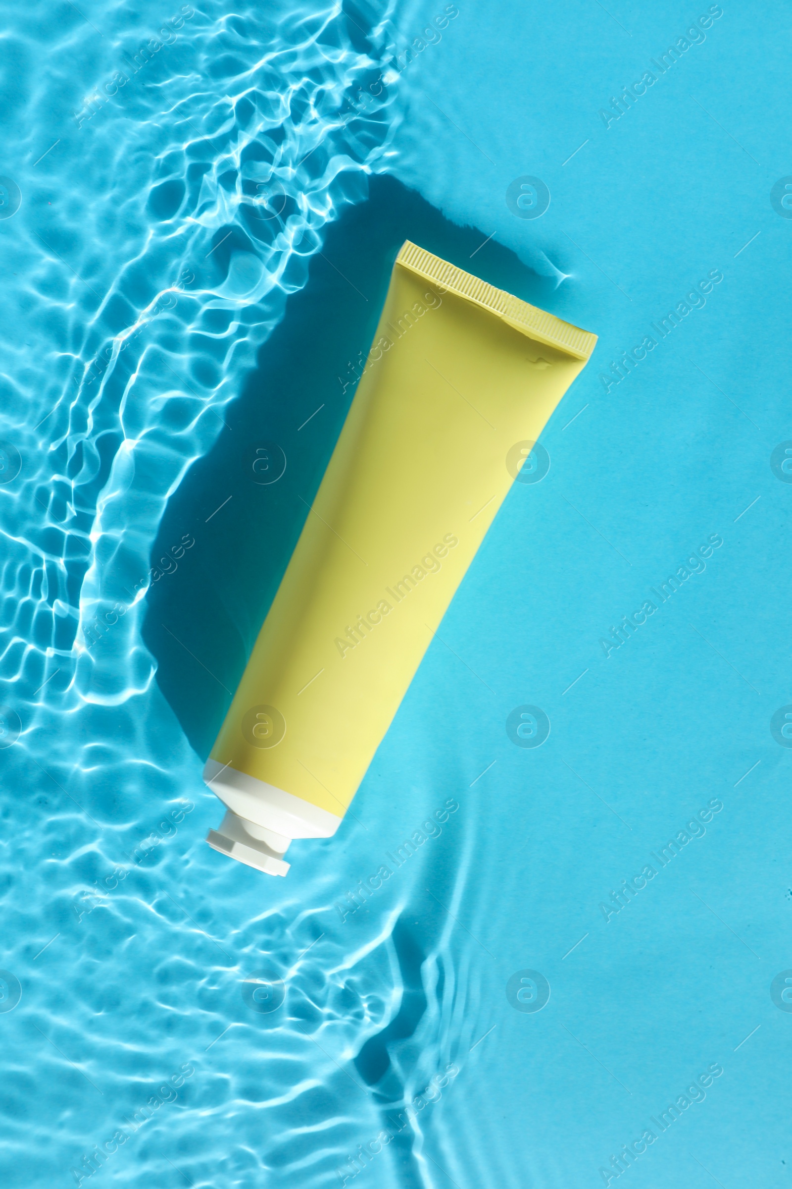 Photo of Tube with moisturizing cream in water on light blue background, top view