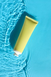 Tube with moisturizing cream in water on light blue background, top view