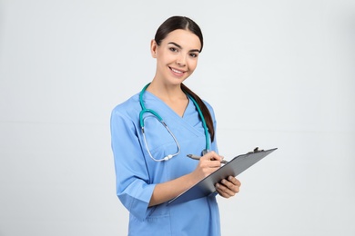 Portrait of medical assistant with stethoscope and clipboard on light background