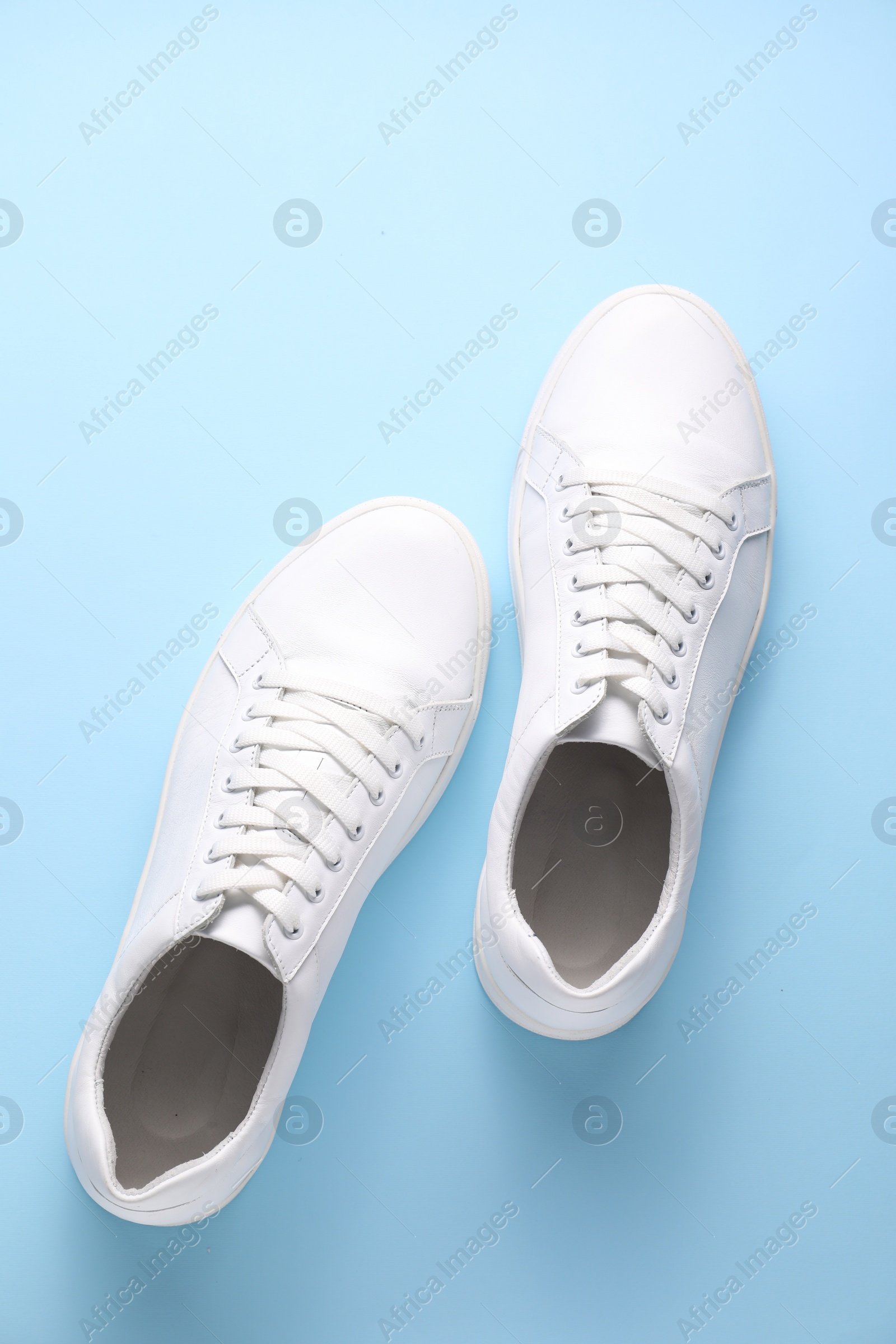 Photo of Pair of stylish white sneakers on light blue background, top view