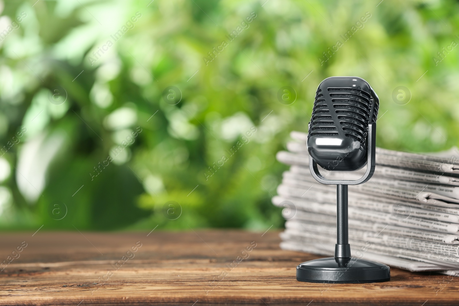 Photo of Newspapers and vintage microphone on wooden table against blurred green background, space for text. Journalist's work