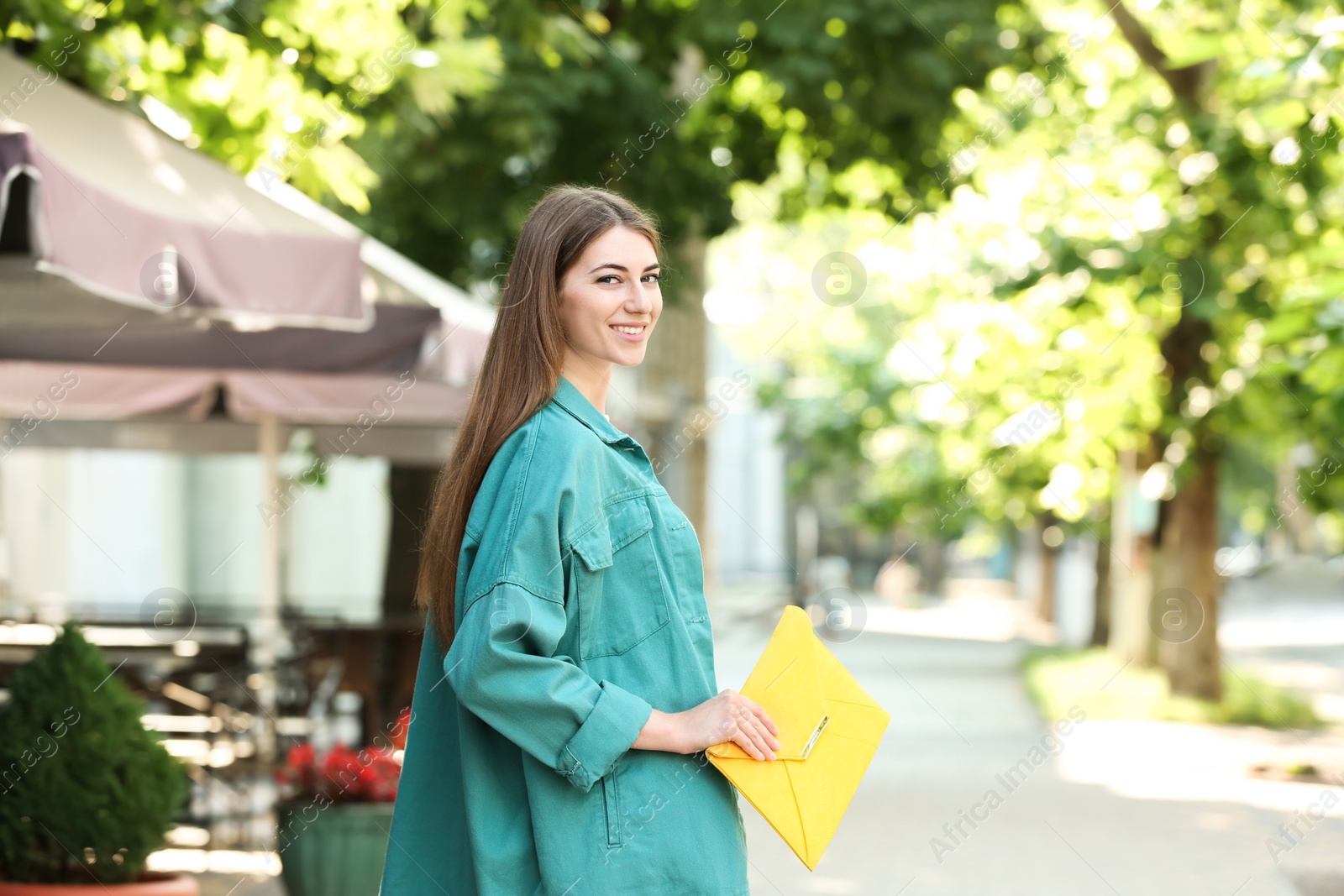 Photo of Beautiful young woman with elegant envelope bag outdoors on summer day