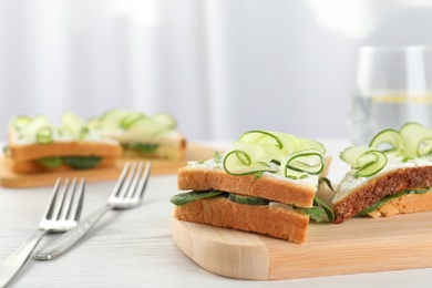 Photo of Wooden board with traditional English cucumber sandwiches on table. Space for text