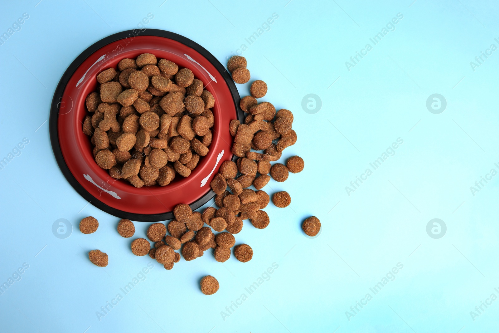 Photo of Dry dog food and feeding bowl on light blue background, flat lay. Space for text