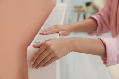 Photo of Woman warming hands on heating radiator indoors, closeup
