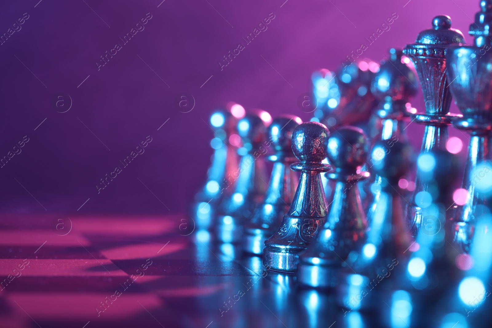 Photo of Chess pieces on checkerboard in color light, selective focus. Space for text