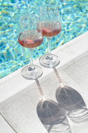 Glasses of tasty rose wine on swimming pool edge