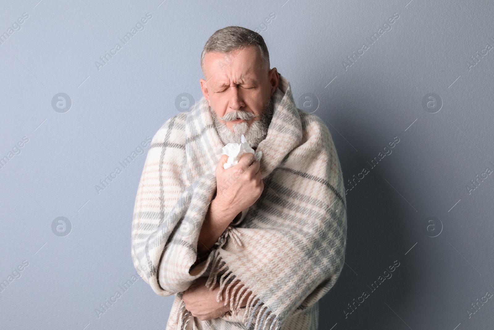 Photo of Mature man wrapped in blanket suffering from cold on color background