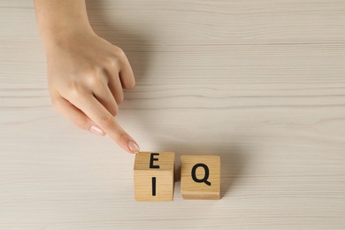 Photo of Woman turning cube with letters E and I near Q at white wooden table, above view. Space for text