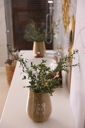 Photo of Vase with beautiful branches near vessel sink in bathroom. Interior design