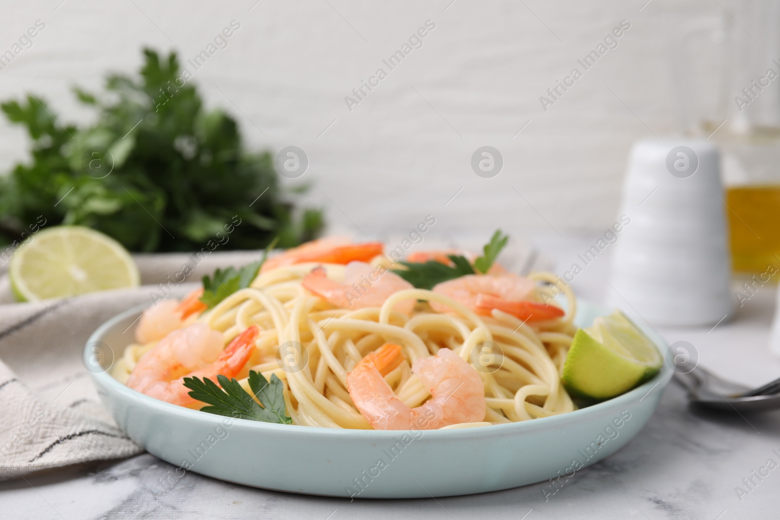 Photo of Tasty spaghetti with shrimps, lime and parsley on white marble table, closeup