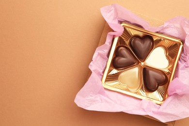 Photo of Partially empty box of chocolate candies on light brown background, top view. Space for text