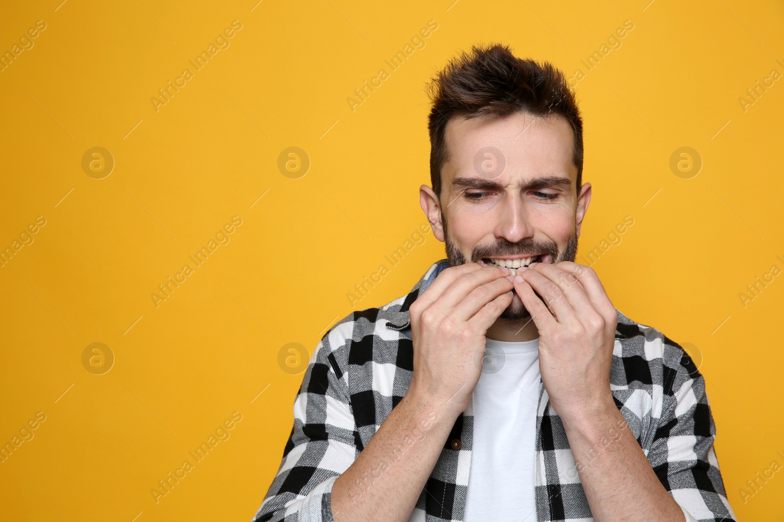 Photo of Man biting his nails on yellow background. Space for text