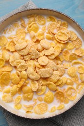 Photo of Bowl of tasty corn flakes on light blue wooden table, top view