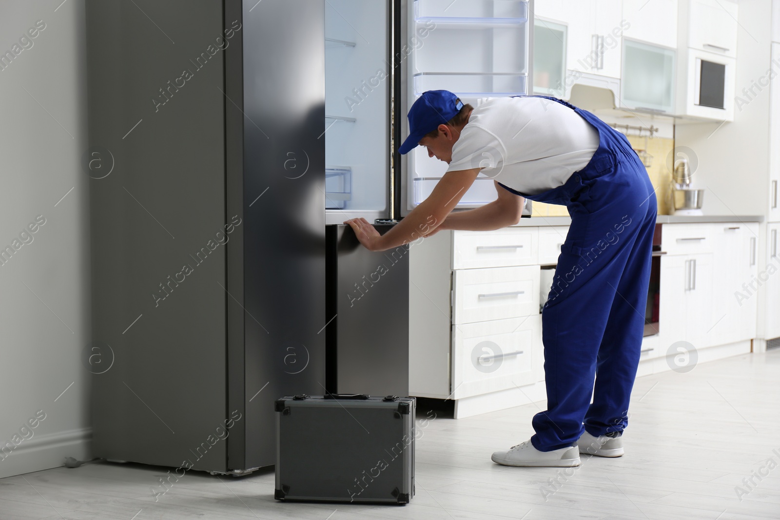 Photo of Male technician with screwdriver repairing refrigerator in kitchen