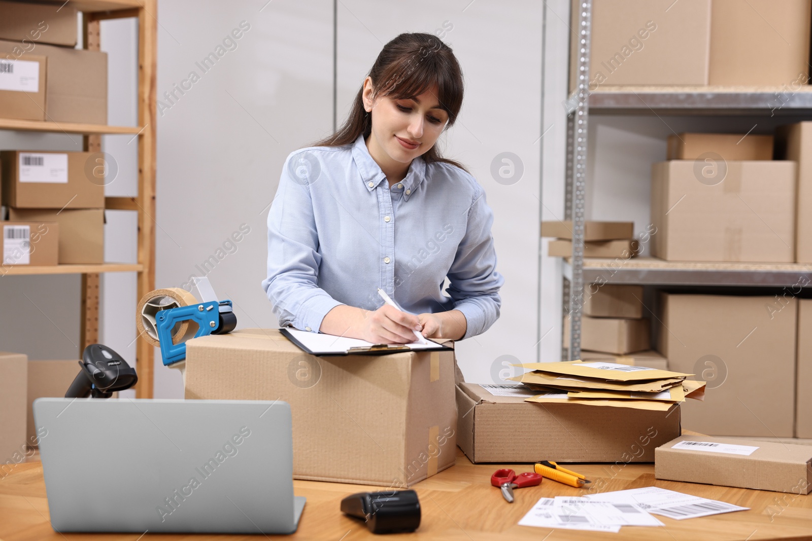 Photo of Parcel packing. Post office worker with clipboard writing notes at wooden table indoors