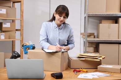 Photo of Parcel packing. Post office worker with clipboard writing notes at wooden table indoors