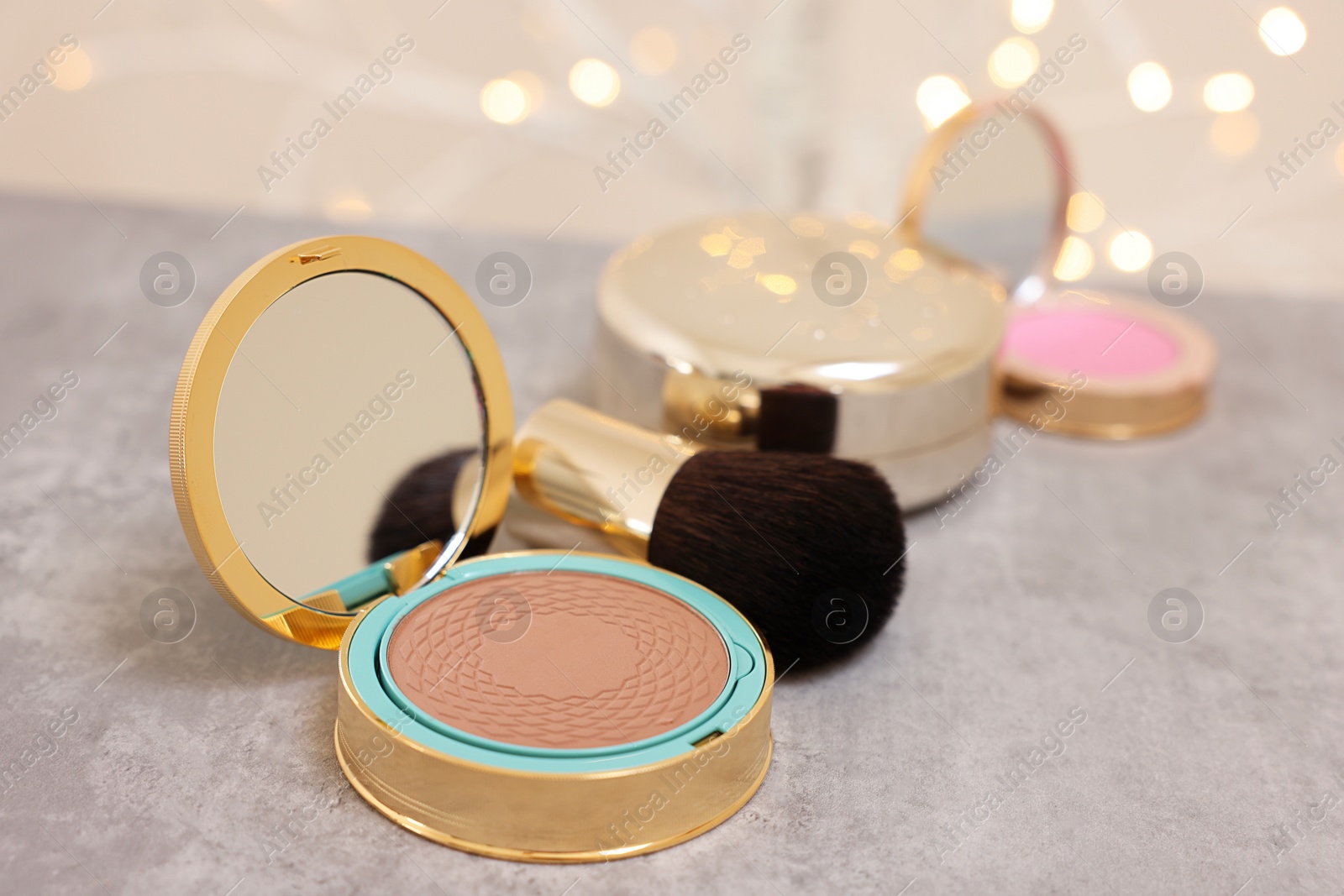 Photo of Face bronzer and makeup brush on grey textured table against blurred lights, closeup
