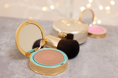 Face bronzer and makeup brush on grey textured table against blurred lights, closeup