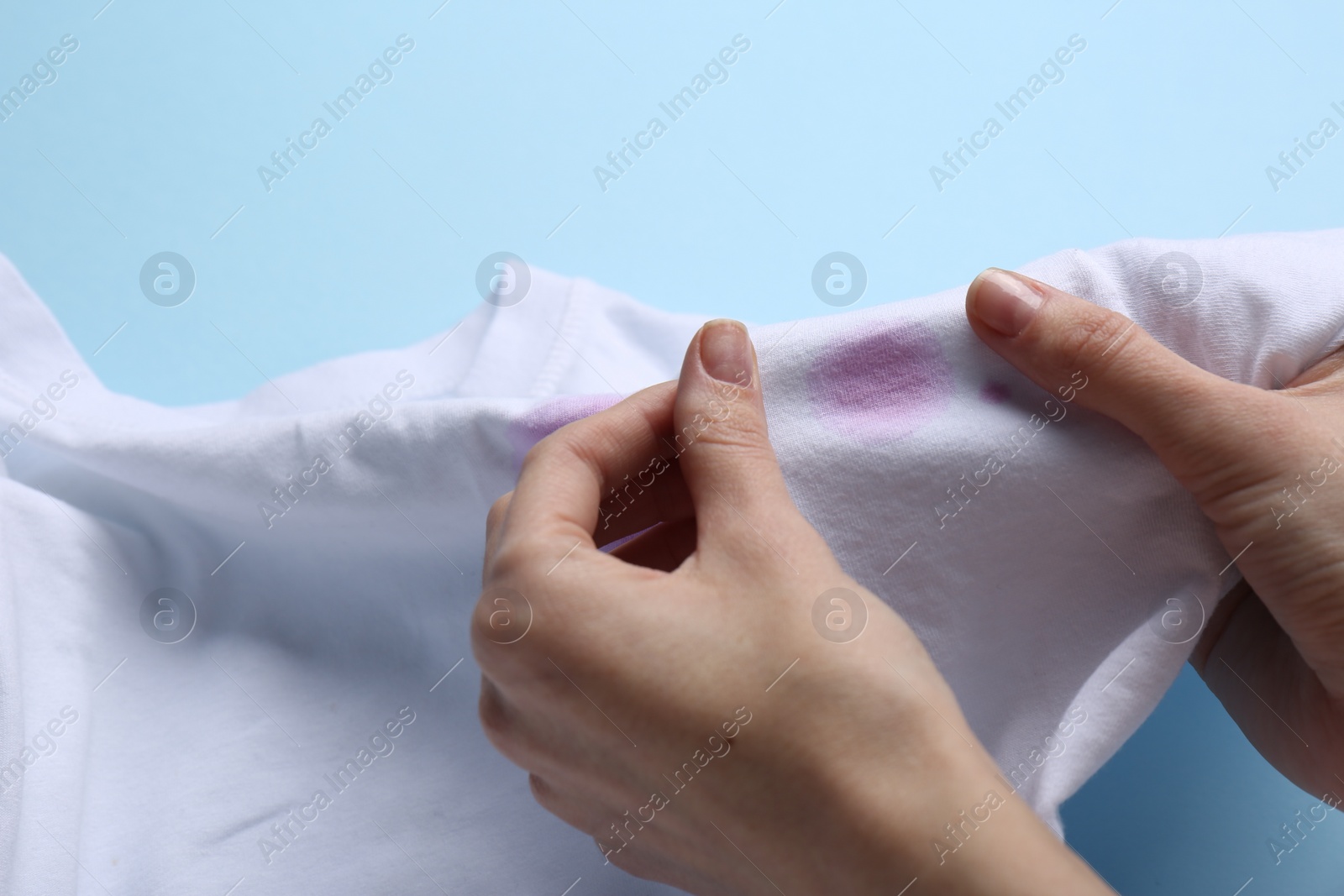 Photo of Woman holding white shirt with purple stain on light blue background, closeup