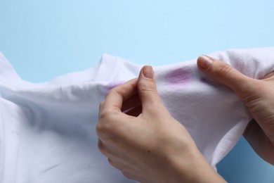 Woman holding white shirt with purple stain on light blue background, closeup