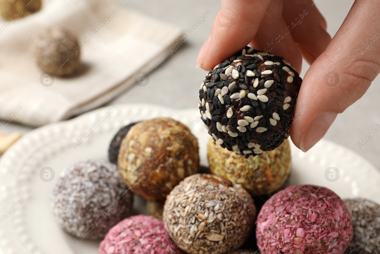 Photo of Woman taking delicious vegan candy ball from plate at table, closeup