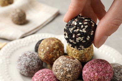 Woman taking delicious vegan candy ball from plate at table, closeup