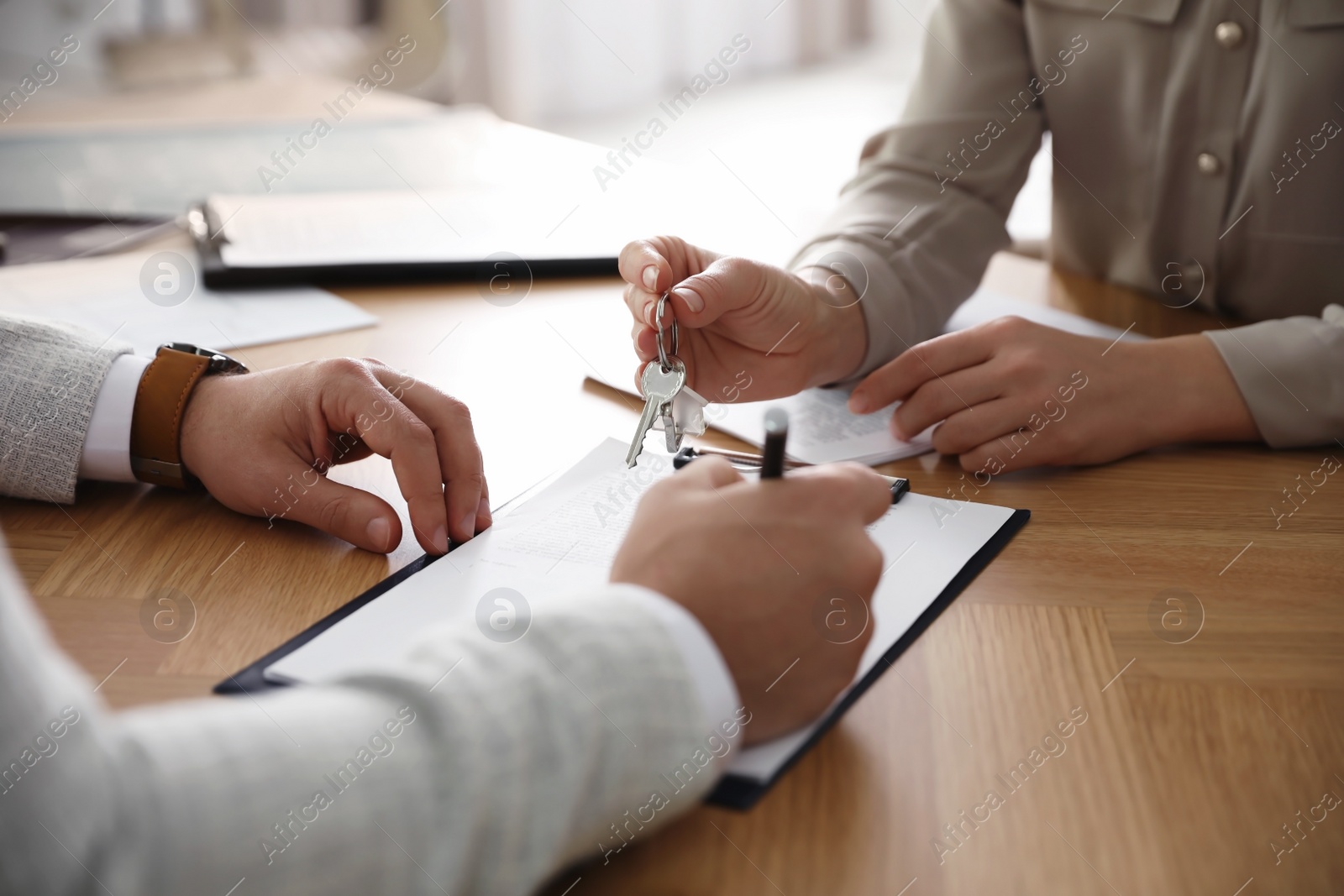 Photo of Real estate agent giving key with trinket to client in office, closeup