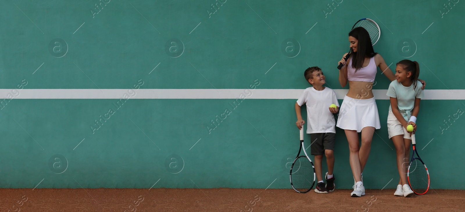 Image of Young woman with her cute children near green wall on tennis court. Banner design with space for text