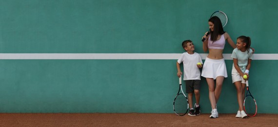 Image of Young woman with her cute children near green wall on tennis court. Banner design with space for text