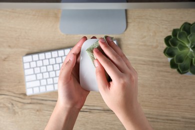 Photo of Woman wiping wireless mouse with paper towel near wooden table, focus on hands