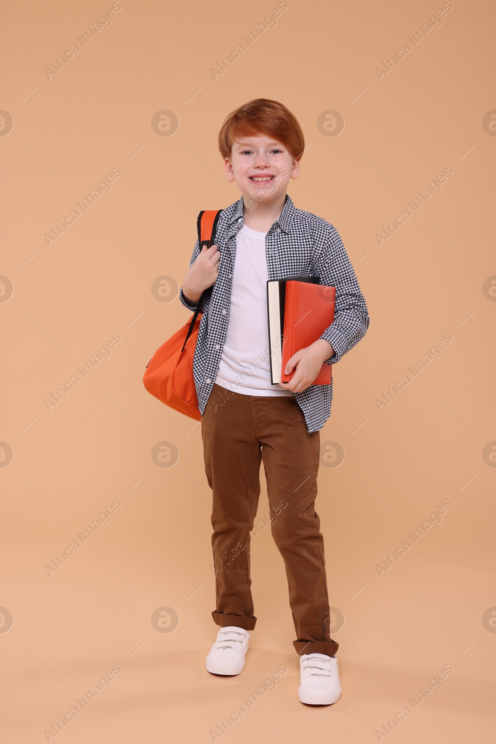 Photo of Smiling schoolboy with backpack and books on beige background