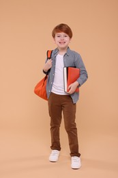 Smiling schoolboy with backpack and books on beige background