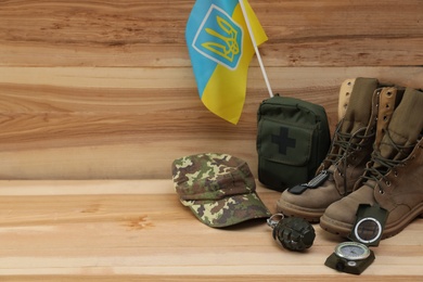 Photo of MYKOLAIV, UKRAINE - SEPTEMBER 26, 2020: Tactical gear and Ukrainian flag on wooden background. Space for text