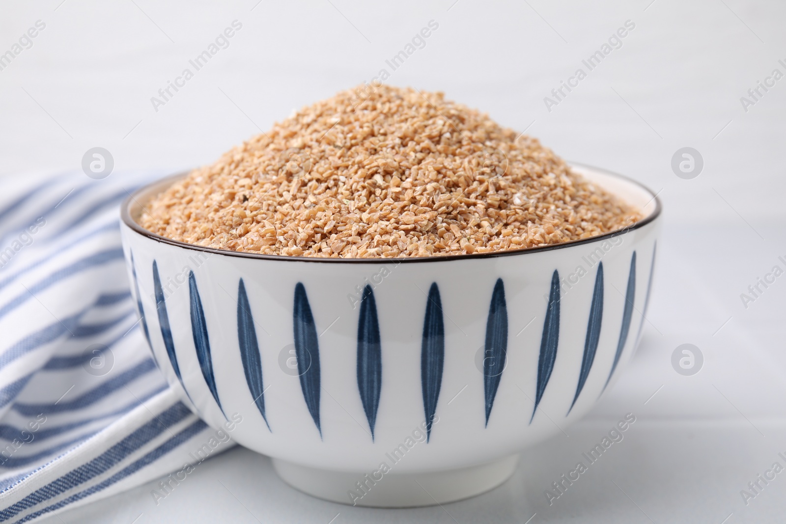 Photo of Dry wheat groats in bowl on white table, closeup