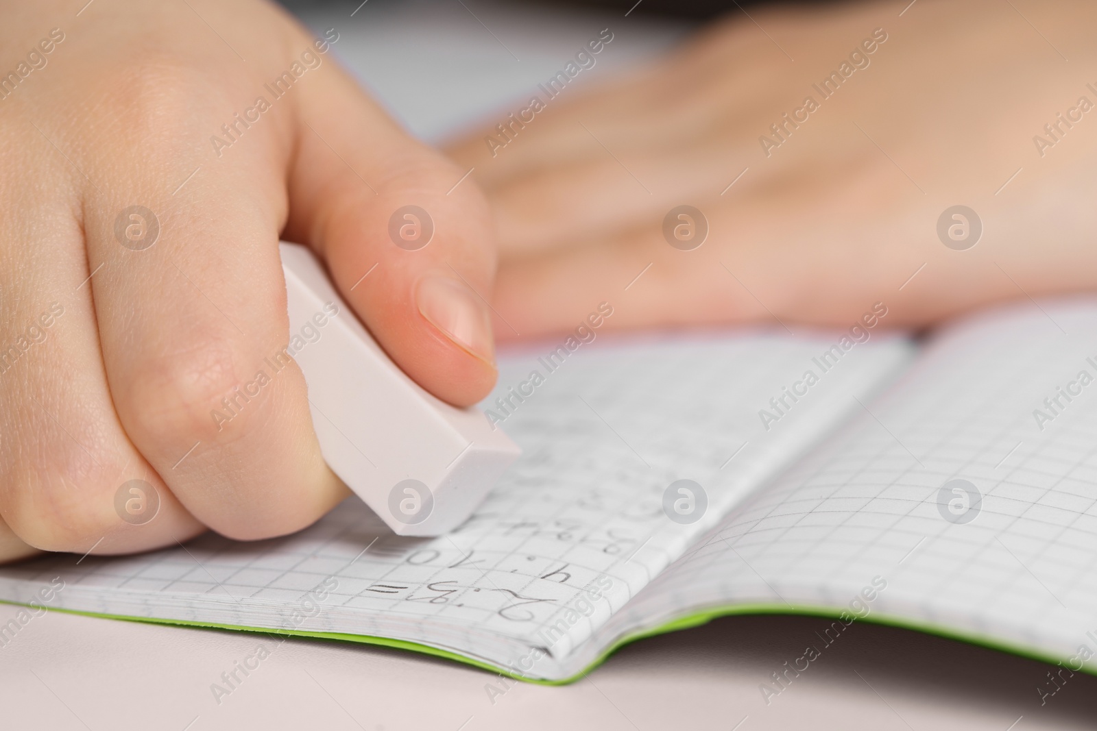 Photo of Boy erasing mistake in his notebook at white desk, closeup