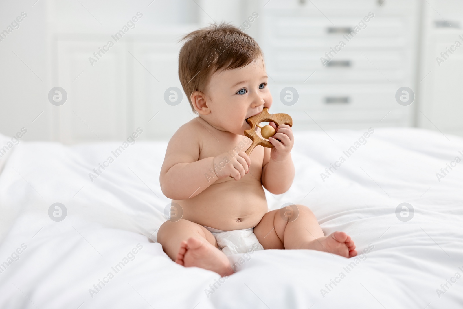 Photo of Cute baby boy with wooden rattle on bed at home