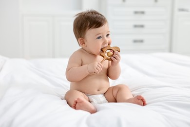 Cute baby boy with wooden rattle on bed at home