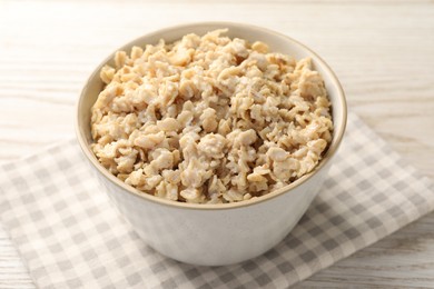 Photo of Tasty boiled oatmeal in bowl on light wooden table, closeup