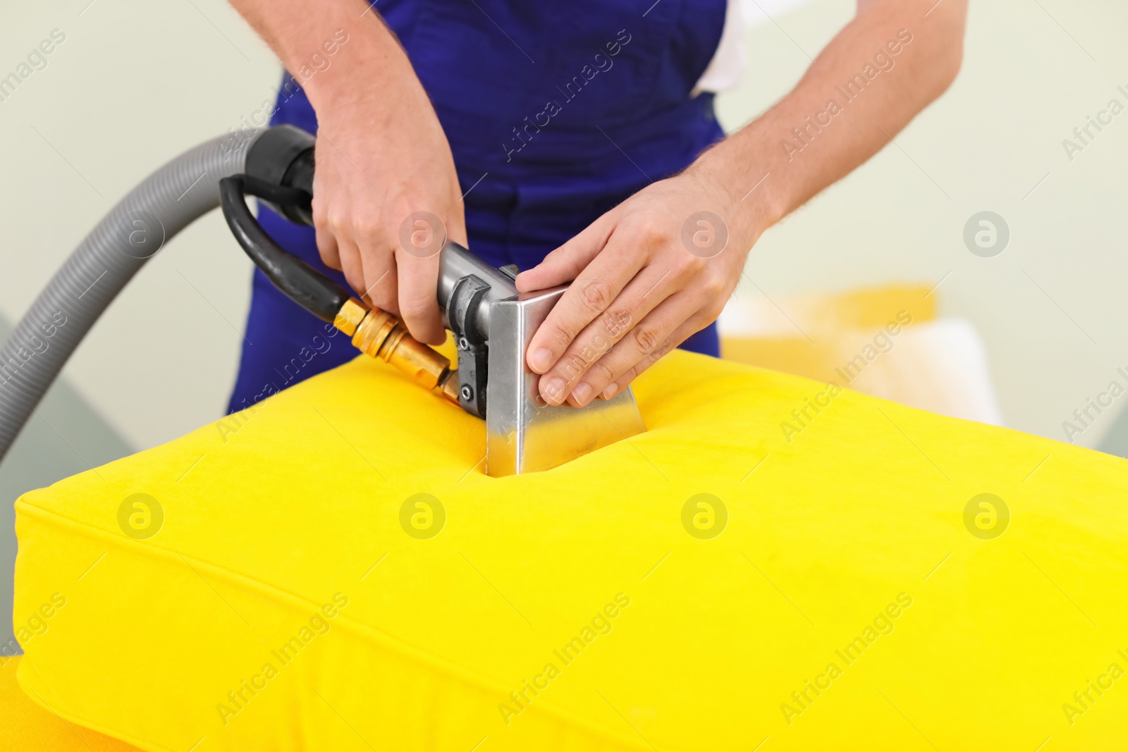 Photo of Dry cleaning worker removing dirt from sofa cushion indoors