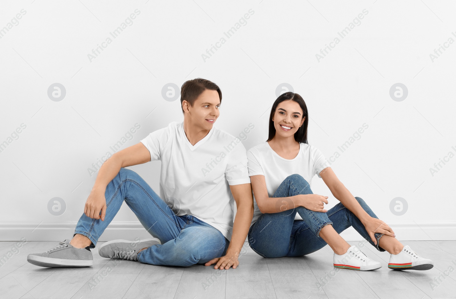 Photo of Young couple in stylish jeans sitting near white wall