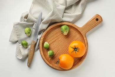 Cutting board with Brussels sprouts, tomatoes and knife on white wooden table, flat lay
