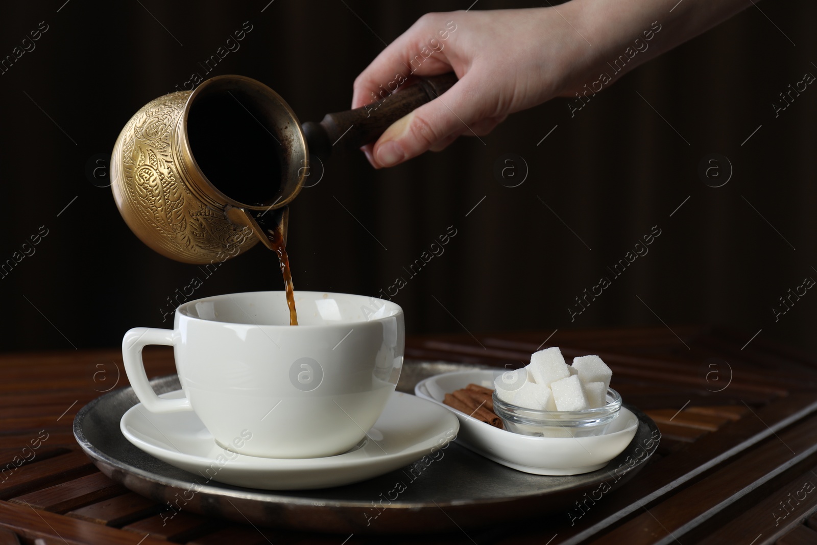 Photo of Turkish coffee. Woman pouring brewed beverage from cezve into cup at wooden table, closeup