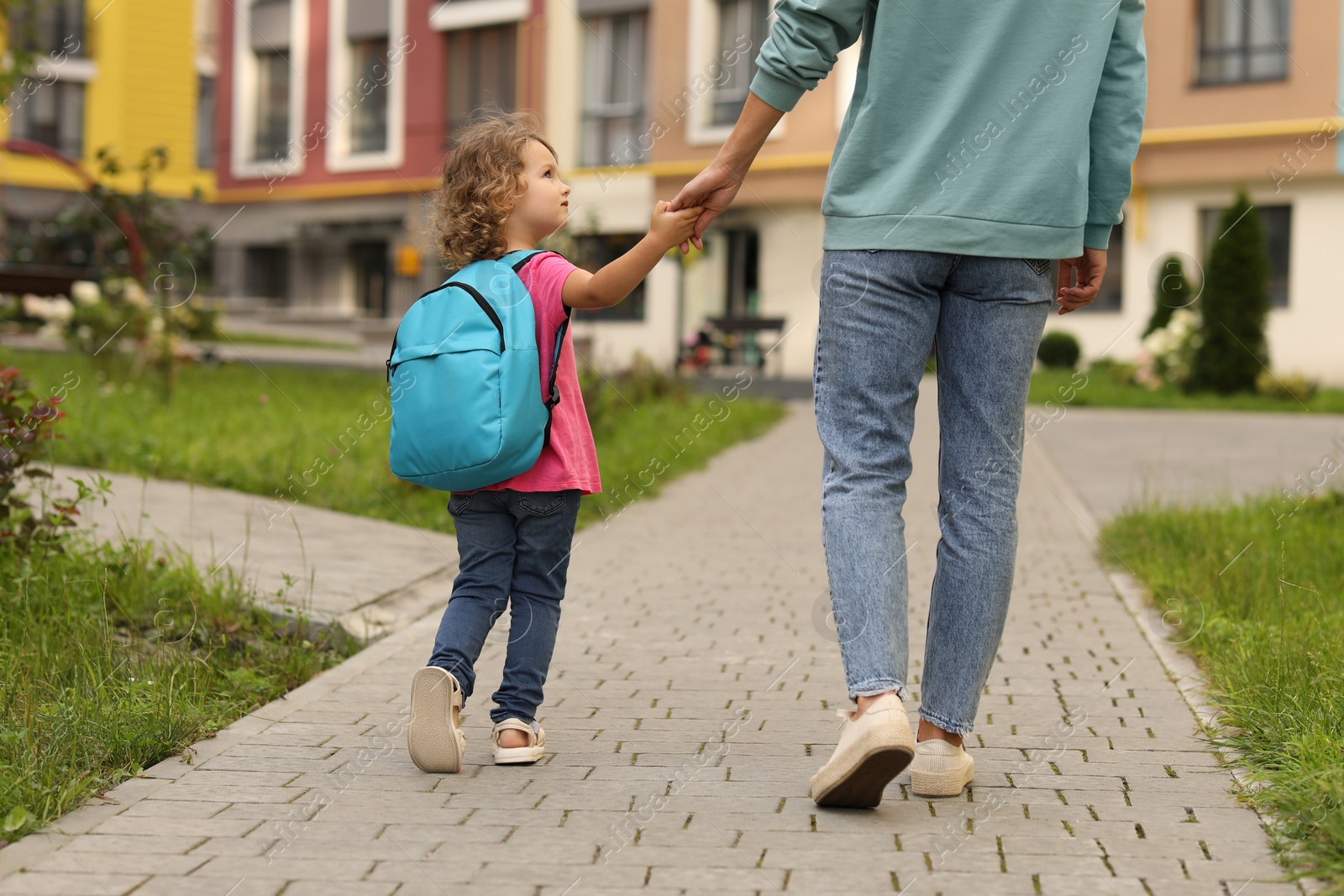 Photo of Woman and her little daughter on their way to kindergarten outdoors, back view