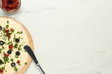 Photo of Fresh butter board with cut olives, sun-dried tomatoes and knife on white marble table, flat lay. Space for text