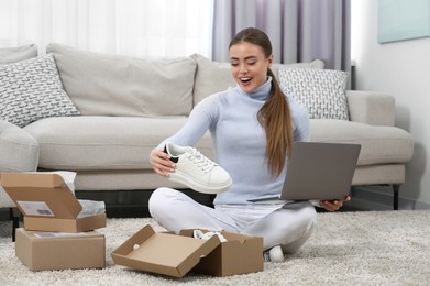 Emotional woman with laptop unpacking parcels at home. Online store