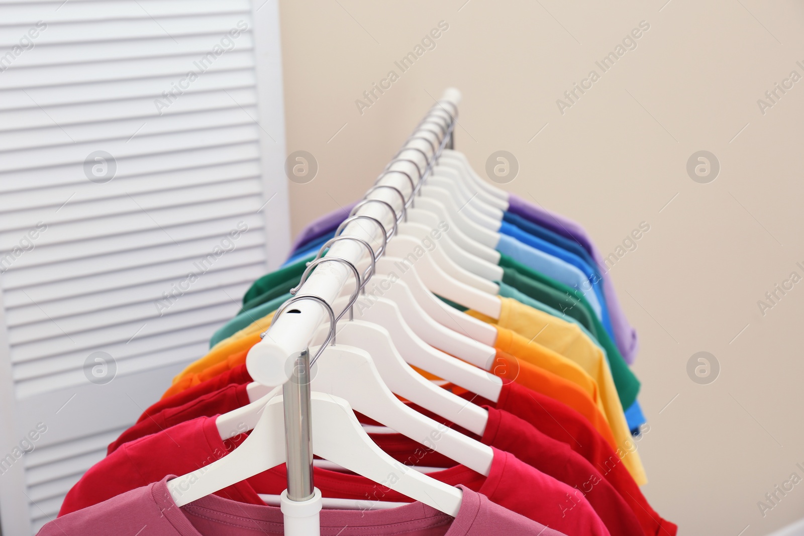 Photo of Rack with bright clothes in room. Rainbow colors