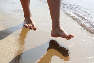 Photo of Woman walking on sandy seashore, closeup of legs