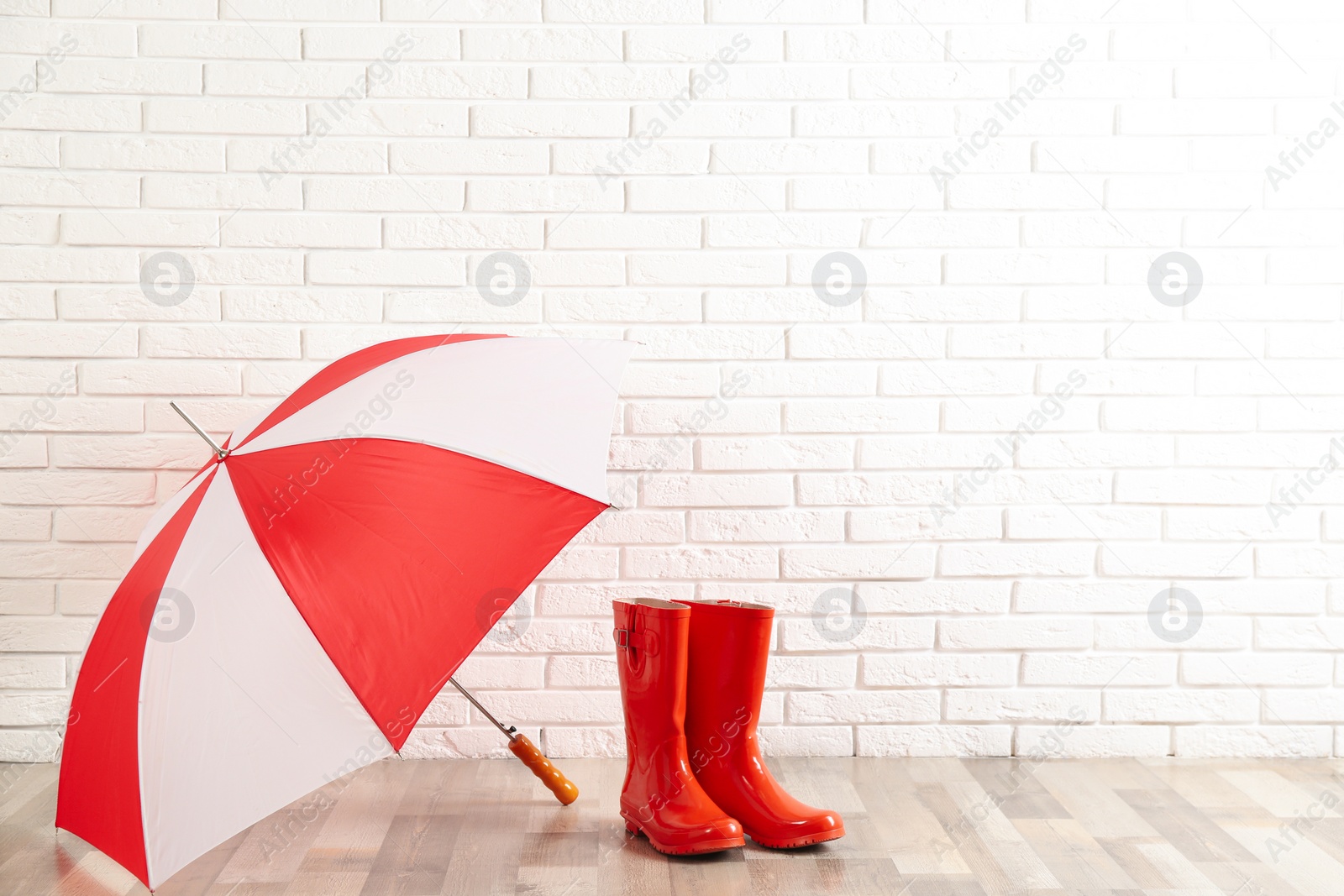 Photo of Beautiful colorful umbrella and rubber boots near white brick wall. Space for text